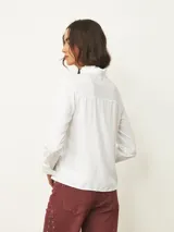 Camisa de manga larga color blanco, con cuello alto tipo mao con detalle de volados y cierre frontal de botones.