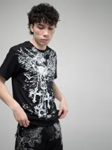 Remera negra de corte oversize con estampado frontal en blanco que presenta motivos góticos, incluyendo alas, cadenas y cruces.
