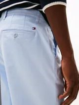 Pantalón chino celeste de pierna recta confeccionado en satén de algodón ligeramente elástico. Cuenta con cierre de cremallera con botón, dos bolsillos ribeteados en la cintura y dos bolsillos traseros de ojal con botón. Presenta detalles distintivos de Tommy Hilfiger y logo bordado en la parte trasera.