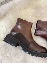 Bota corta de cuero color chocolate con suela track negra. Presenta una combinación de texturas que incluye cuero liso, gamuza y detalles con textura de reptil en la puntera y el talón.