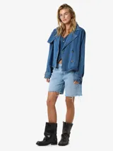 Trench corta de denim azul claro, con cuello solapa estilo biker, doble botonadura frontal y diseño holgado.