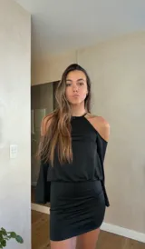 Vestido corto negro con cuello halter, hombros descubiertos y mangas largas acampanadas. Presenta un diseño ajustado en la cintura y falda con frunces laterales.