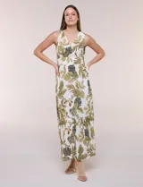 Vestido maxi sin mangas de base blanca con estampado de hojas tropicales en tonos verde y marrón. Presenta escote en V cruzado, cintura elastizada con paneles fruncidos y falda larga fluida con volados en el ruedo.