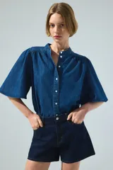 Blusa de denim de algodón suave, de color azul, con cuello mao, botonadura frontal y mangas cortas abullonadas.