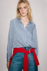 Camisa de cuello solapa y manga larga, con bajo ajustable mediante cordones y cierre frontal con botones ocultos. Diseño a rayas blancas y azules.