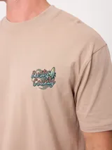Remera oversize color beige de manga corta, con gran estampa colorida en la espalda con diseño de mapa de playa y la inscripción "Rusty County".