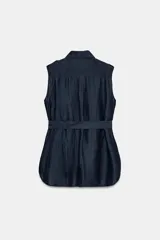 Chaleco azul marino confeccionado en hilatura con lino, con cuello solapa, manga sisa y trabillas en los hombros. Cuenta con bolsillos de plastrón con solapa en el delantero, cinturón ajustable del mismo tejido y bajo asimétrico con aberturas laterales. Cierre frontal con botones.