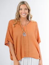 Remerón tipo poncho color naranja confeccionado en lino italiano, con escote en V y bolsillos laterales.