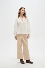 Blusa de viscosa color blanco, con cuello en V, detalles de volados y frunces en el frente, y mangas largas abullonadas con puños ajustados.