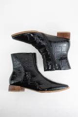 Botinetas de cuero con textura croco acharolado en color negro. Presentan un diseño de punta cuadrada, cierre lateral y un taco bajo de madera.