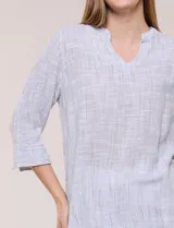 Blusa de silueta relajada con textura tramada, color azul con rayas verticales en tonos rosados, celestes y amarillos. Cuenta con cuello mao abierto en V y mangas tres cuartos amplias con pequeña abertura lateral en el puño.