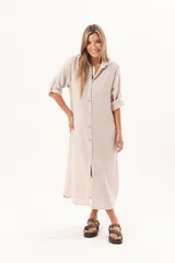Vestido camisero largo de lino color beige, con silueta relajada, abotonado al frente, cuello camisero, mangas regulables y tajos laterales.