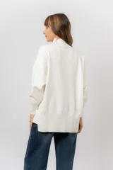 Sweater de tejido de punto color beige, con cuello alto, hombros caídos, mangas largas con puños acanalados y tajos laterales en el ruedo.