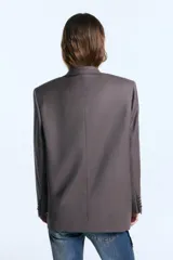 Blazer de corte oversize confeccionado en sarga, con hombreras marcadas, solapas clásicas y cierre frontal con un botón forrado a tono. Presenta dos bolsillos delanteros con solapa, logo bordado en una de las tapas y bordado decorativo en el cuello trasero. El diseño cuenta con un largo irregular que llega por debajo de la cadera y está completamente forrado.