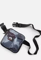 Morral Rip Curl con diseño de camuflaje en tonos gris y negro, de formato cuadrado, con múltiples bolsillos frontales, correa de hombro ajustable y parche con logo de la marca.