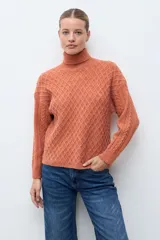 Polera de tejido de punto color ocre con cuello alto, diseño de rombos en relieve en el frente y mangas con detalle de trenzas laterales.