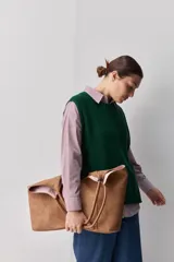 Chaleco tejido de punto color beige, con cuello redondo, terminaciones en rib y lazos laterales regulables que permiten ajustar la prenda.