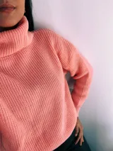 Sweater de punto grueso color salmón, con cuello alto y mangas largas.