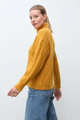 Polera de tejido de punto color ocre con cuello alto, diseño de rombos en relieve en el frente y mangas con detalle de trenzas laterales.