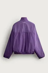 Cazadora relaxed fit de denim de algodón en color violeta, con efecto lavado, cuello alto, cierre frontal de cremallera y bolsillos en las costuras laterales. Presenta puños y dobladillo elásticos.