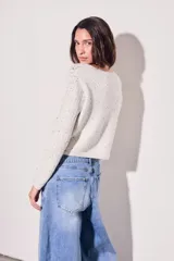 Cardigan de punto color beige claro con motas oscuras (tweed), manga larga y escote en V. Se cierra mediante lazos cruzados en el frente.