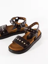 Sandalias marrones de cuero con plantilla anatómica forrada en cuero, acceso mediante pulsera regulable con velcro y detalle de tachas plateadas.