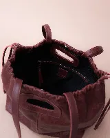 Cartera tipo tote de cuero color bordó, con diseño fruncido en los laterales y abertura central integrada como asa. Presenta una silueta flexible y espaciosa, ideal para uso diario.