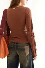 Top de manga larga color marrón, confeccionado en tejido acanalado con cuello bote. Presenta costuras decorativas expuestas a lo largo de las mangas, creando un efecto de relieve.