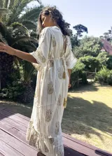 Túnica larga de estilo boho, color crudo con estampado de arabescos y detalles en hilo dorado. Presenta escote en V, mangas amplias tipo kimono y cordón ajustable en la cintura con borlas decorativas.