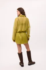 Vestido corto de chiffon color verde lima, con transparencia, cuello camisero, botones frontales y elástico en la cintura. Las mangas son largas y abullonadas con puños elásticos.