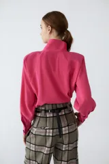 Camisa fucsia de cupro con cuello alto y cartera cruzada en delantero con abotonado de snaps soft-touch. Tiene terminación redondeada con pequeños tajos en los laterales.