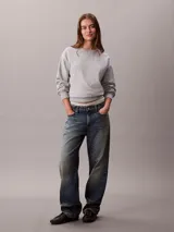 Buzo de felpa francesa gris claro, de cuello redondo y manga larga, con puños y dobladillo acanalados. Presenta un diseño holgado y lleva el logo retro de Calvin Klein bordado discretamente en el pecho.
