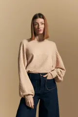 Sweater color crema con mangas abullonadas y puños elastizados. Presenta una textura tejida en relieve con patrón de ladrillos en el cuerpo y rayas horizontales en las mangas.