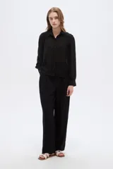 Camisa negra de poliéster con detalles de lurex y textura en relieve, corte holgado, mangas largas con puños y cierre frontal con botones.