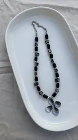 Collar de piedra reconstruida negra, nácar teñido negro, hematite plateado y dije grande de flor en acero quirúrgico.