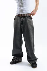 Pantalón de denim azul desgastado, corte mega baggy con piernas anchas y bolsillos traseros grandes. Presenta un bordado dorado en estilo gótico en el bolsillo trasero izquierdo.