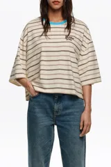 Remera boxy de algodón orgánico a rayas horizontales en tonos beige, marrón y blanco, con cuello redondo en color celeste brillante y logo bordado en el pecho.