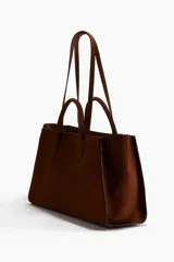 Cartera tote color marrón con doble asa de mano y correas finas para el hombro. Cuenta con cierre de mosquetón en el interior y un compartimento interior con cierre.