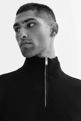 Buzo negro de tejido de punto suave, con cuello alto y medio cierre metálico. Presenta un corte estándar y manga larga con puños y bajo rectos.