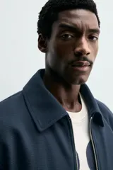 Cazadora boxy fit color azul marino, confeccionada en tejido de algodón. Presenta cuello solapa, manga larga con puño abotonado, bolsillos de vivo en la cadera y bajo elástico. Cierre frontal con cremallera.