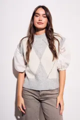 Chaleco de tejido de punto con diseño de rombos en tonos gris claro y blanco. Presenta mangas abullonadas de tela blanca con detalles de encaje y cuello redondo.