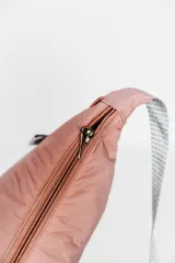 Bandolera color gris claro con forma de media luna, cierre de cremallera y correa ajustable. Incluye etiqueta metálica con el logo de la marca.