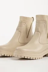 Bota tipo chelsea de caña media en color beige, con suela track dentada y paneles laterales elásticos acanalados.