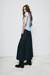 Falda midi de denim azul oscuro con tiro medio, bolsillos delanteros y costuras a contraste. Presenta un diseño con canesú estructurado y falda con frunces, cierre frontal con cremallera y botón metálico.