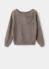 Jersey de punto grueso en color gris, con cuello barco que deja un hombro al descubierto, manga larga y diseño recto. Presenta un detalle de cristales bordados en la parte superior delantera.