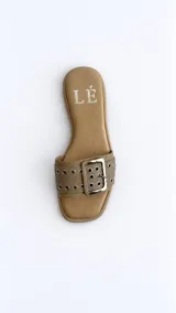 Sandalias planas color tostado, con una tira ancha en el empeine decorada con ojalillos metálicos y una hebilla grande central.