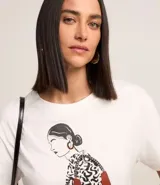 Remera blanca de algodón con mangas cortas y estampa de una mujer con un vestido estampado y un bolso rojo.