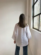 Camisa blanca de lino, con cuello en V, cierre frontal de botones y mangas amplias de corte holgado.