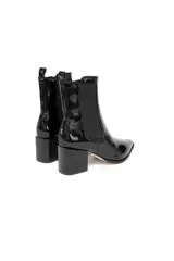 Botas de caña baja tipo chelsea de cuero charol negro con acabado brillante, punta fina y taco cuadrado. Cuentan con paneles elásticos laterales y presilla trasera.