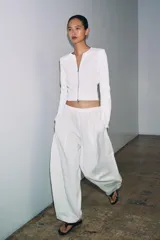 Chaqueta de punto liso color blanco, con cuello redondo, manga larga acabada con cremalleras en los puños y cierre frontal con cremallera.